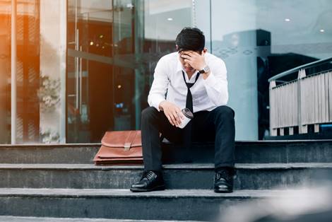 man sitting on steps of office building stressed - Wrongful Termination